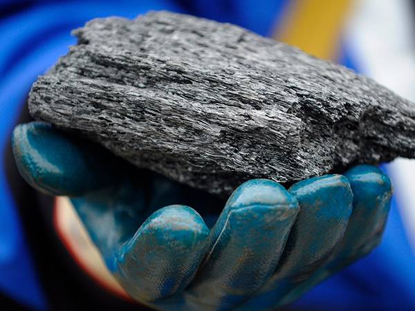 A piece of needle coke is held in the hand of a factory worker.